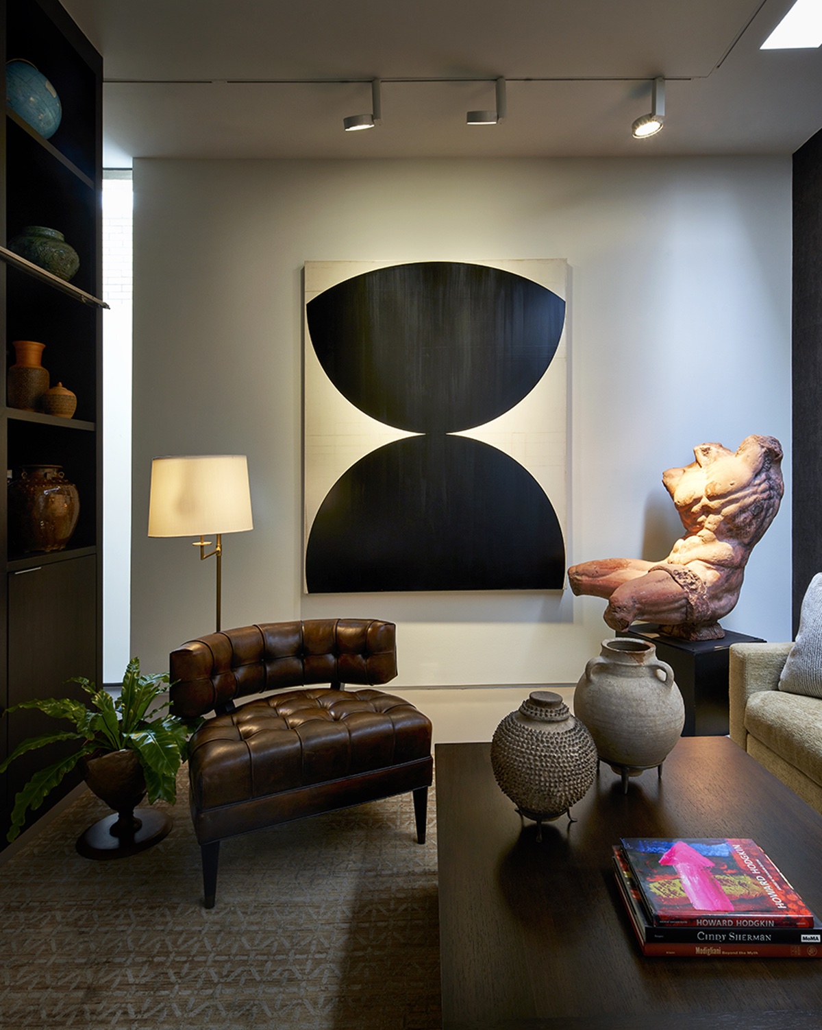 lounge area with tufted brown leather chair in front of abstract black and white painting